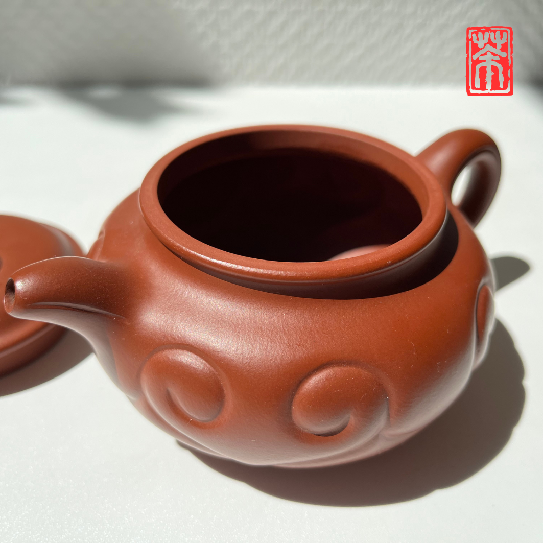 Ergänzen Sie Ihre Teekollektion mit dieser eleganten Yixing-Teekanne aus rötlichem Zisha-Ton. Die lebendige, helle Tonfarbe und das kunstvoll eingearbeitete Wolkenrelief machen sie zum Blickfang – perfekt, um die erdigen Aromen von Pu-Erh und dunklen Tees stilvoll zu genießen.